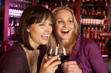 Two Women Enjoying Drink Together In Bar Looking Away From Camera Smiling